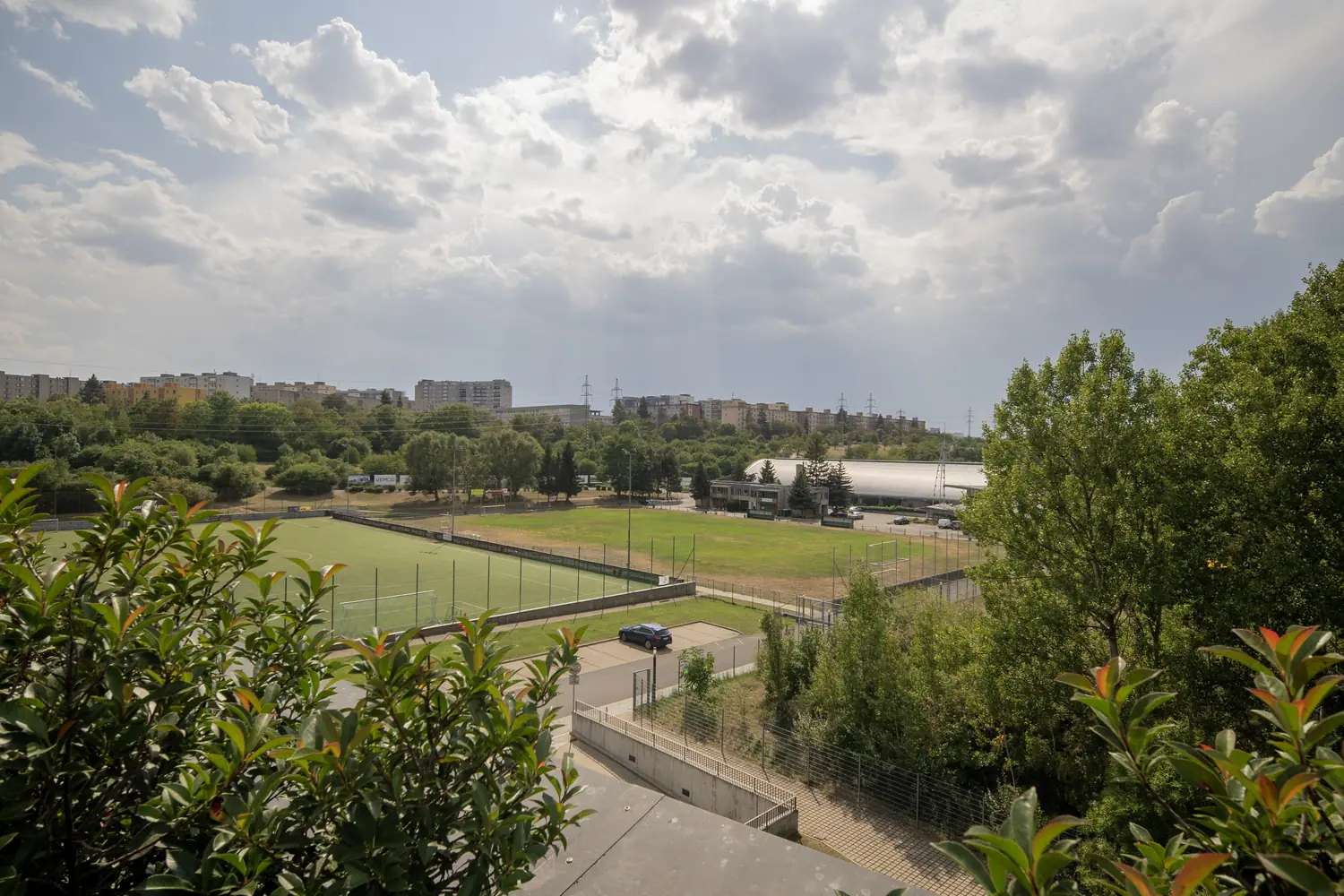 Výhled ze střešní terasy na zeleň a sportovní areál v sousedství